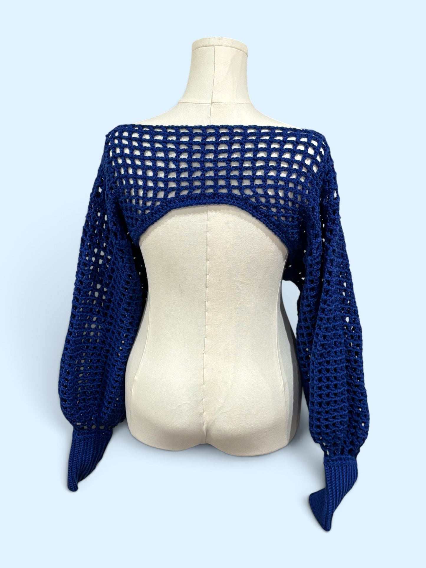Nana's Cottage navy blue handmade crochet bolero shrug with open back and voluminous balloon sleeves on a mannequin.